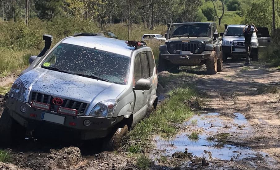 Todoterreno plateado salpicado de barro en primer plano, con más vehículos detrás en una pista encharcada.