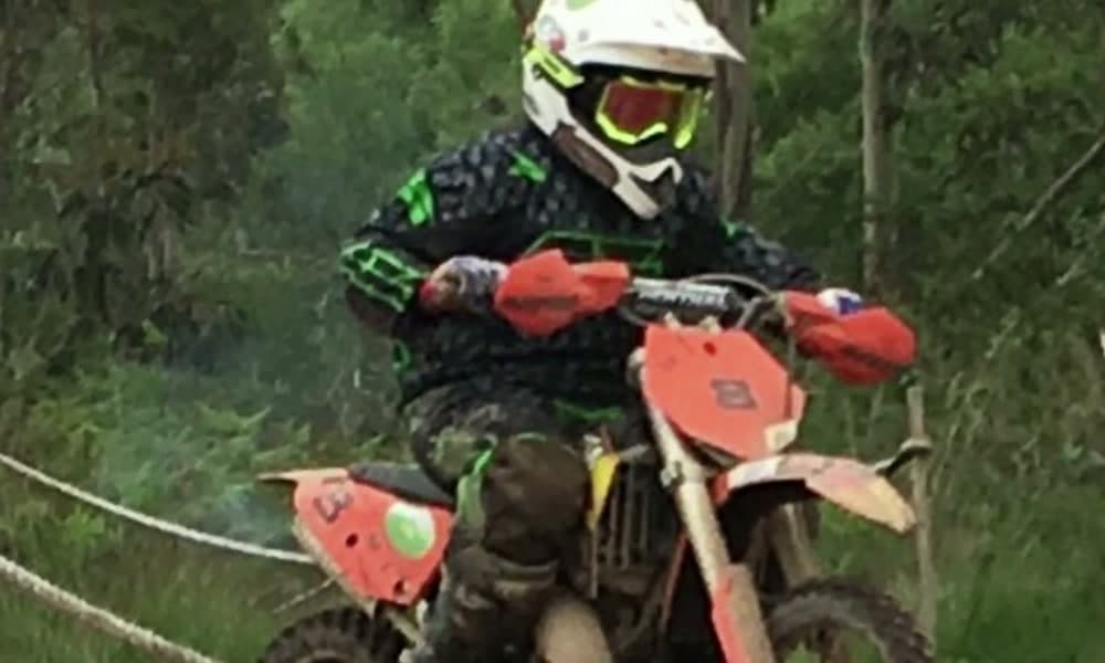 Piloto con casco y peto atravesando la vegetación en una moto de enduro roja.