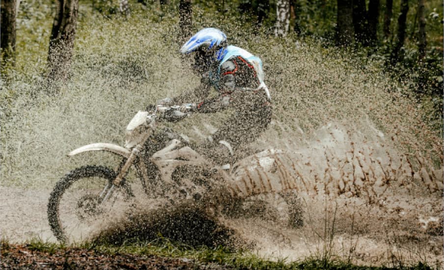 Moto de enduro derrapando en un charco de barro y levantando una cortina de agua y tierra.