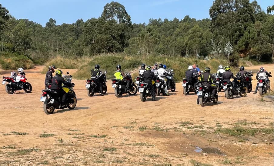 Una docena de motos trail con sus pilotos, paradas en la explanada de tierra antes de salir.