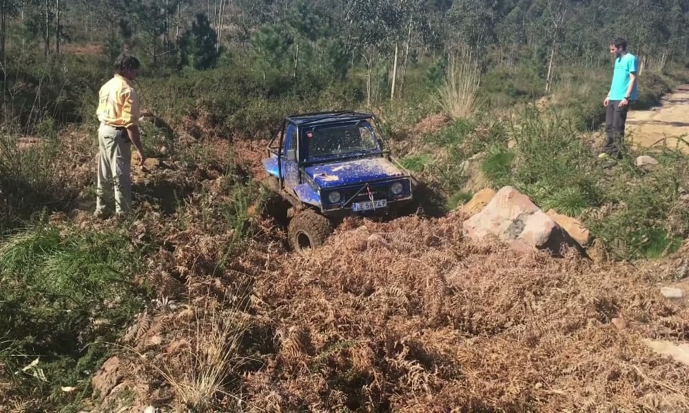 Todoterreno azul cruzando una zona de helechos secos y piedra suelta, con dos monitores siguiendo la maniobra a pie.
