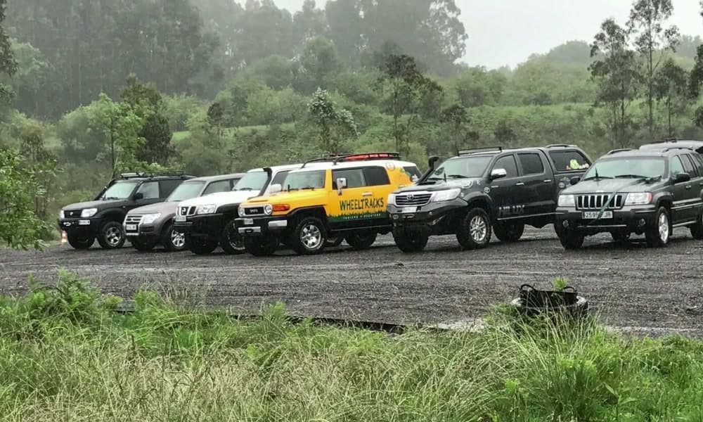 Fila de todoterrenos aparcados en la explanada de grava a primera hora, con bruma sobre el valle.
