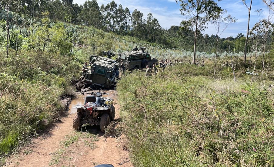 Dos vehículos militares de la colección del parque y un quad en una pista entre helechos y matorral.