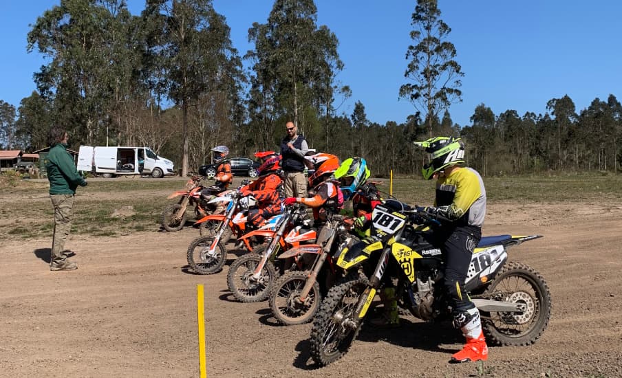 Fila de motos de cross con sus pilotos en la línea de salida de la pista de tierra.